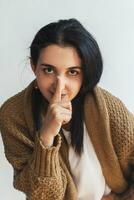 Silence gesture. Portrait of a young cute woman in sweater saying please keep calm sign photo