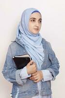 Portrait of cute Muslim businesswoman. Attractive Muslim student holding notepads. Lovely Muslim girl in hijab and denim jacket. Modern, cultural, religious and business concept photo