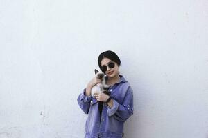 Young attractive woman hugging pussy cat in hands. Cute and glamorous girl in trendy sunglasses posing with her Siamese cat photo