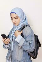 Modern Muslim student girl listens to music, podcasts, and audiobooks on the smartphone. Happy Muslim woman in hijab listening songs with the headphone photo