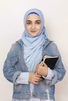 Portrait of cute Muslim businesswoman. Attractive Muslim student holding notepads. Lovely Muslim girl in hijab and denim jacket. Modern, cultural, religious and business concept photo