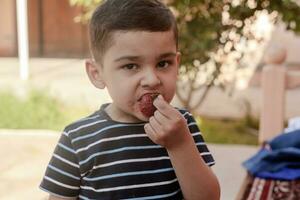un pequeño chico comiendo fresas verano alimento. un joven niño come un sabroso fresa en caliente verano día foto