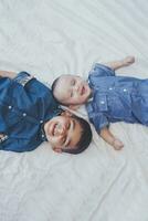 contento infancia concepto. contento hermanos retrato. 6 6 años chico y 6 6 meses antiguo bebé chico teniendo divertida. dos pequeño niños sonriente a el cámara. linda pequeño hermanos acostado en cama juntos foto