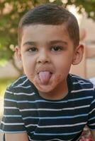 Little boy contorts his face at outdoors. 6 years old kid in summer holidays. Cute little boy fooling around. People, childhood lifestyle concept. Portrait of young child making funny faces photo