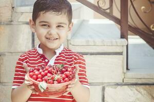 Cute little boy smiling and holding a bowl of freshly picked cherry berries. Copy space. Childhood and summertime concept photo