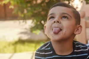 Little boy contorts his face at outdoors. 6 years old kid in summer holidays. Cute little boy fooling around. People, childhood lifestyle concept. Portrait of young child making funny faces photo