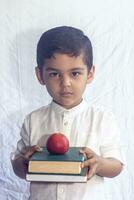 espalda a colegio concepto. linda medio oriental chico participación un apilar de libros en contra el blanco antecedentes. retrato de central asiático niño preparando a Vamos a colegio foto