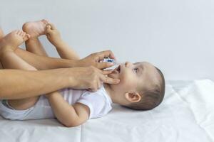 Little boy getting nasal drops. Pediatrician putting saline drops in infant's nose. Mother hands clearing the nose of baby. 6-month baby boy gets nose drops. photo