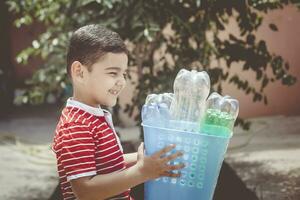 Plastic pollution. Little boy collected plastic bottles and holding recycling bin. Free space photo