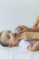 Little boy getting nasal drops. Pediatrician putting saline drops in infant's nose. Mother hands clearing the nose of baby. 6-month baby boy gets nose drops. photo