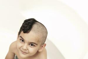 Six-year boy at haircutting at home. Father cut half of the son's hair off at the bathroom photo