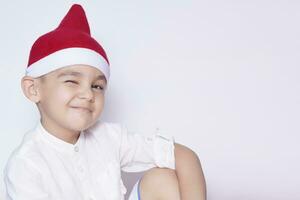 Portrait of handsome 6-7 year old middle-eastern child in Santa hat. Little cute kid smiling and winking. Celebrating Christmas photo