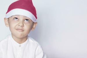 hermoso niño con Papa Noel gorra deseando o soñando algo. niño soñando acerca de Navidad regalo. niño mirando arriba y pensando foto