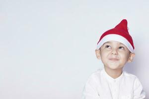 hermoso niño con Papa Noel gorra deseando o soñando algo. niño soñando acerca de Navidad regalo. niño mirando arriba y pensando foto