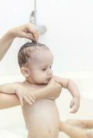 Young mom washing her baby boy's hair at bathroom. Mother bathing her baby photo