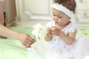 Baby girl in white dress taking a beautiful single white flower photo