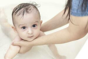 Young mom washing her baby boy's hair at bathroom. Mother bathing her baby photo