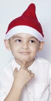 hermoso niño con Papa Noel gorra deseando o soñando algo. niño soñando acerca de Navidad regalo. niño mirando arriba y pensando foto