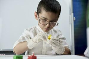 A kid in glasses and gloves playing with plasticine photo