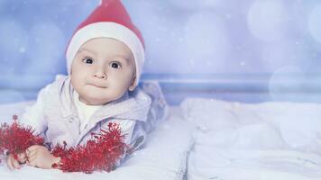 pequeño gracioso Papa Noel chico jugando con Navidad o nuevo año fiesta festivo guirnalda. 1 año antiguo bebé chico en Papa Noel claus gorra. foto
