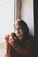 Cold autumn days - young multi-racial female drinks coffee in a cozy windowsill photo