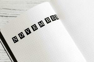 Filling in the diary, writing November in a notebook in a dot photo