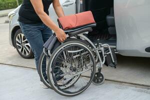 asiático invalidez mujer en silla de ruedas consiguiendo en su auto, accesibilidad concepto. foto