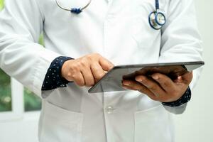 Asian smart man doctor holding digital tablet technology to search knowledge solve treatment for patient in hospital. photo