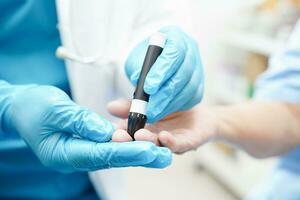 Asian doctor using lancet pen on senior patient finger for check sample blood sugar level to treatment diabetes. photo