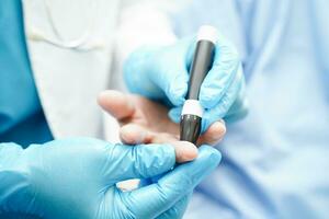 Asian doctor using lancet pen on senior patient finger for check sample blood sugar level to treatment diabetes. photo