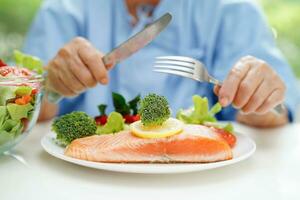 Asian elderly woman patient eating salmon stake and vegetable salad for healthy food in hospital. photo
