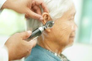 Otolaryngologist or ENT physician doctor examining senior patient ear with otoscope, hearing loss problem. photo