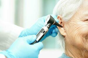 otorrinolaringólogo o ent médico médico examinando mayor paciente oído con otoscopio, escuchando pérdida problema. foto