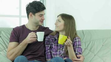 Couple looking at each other while sitting on a sofa with cups video