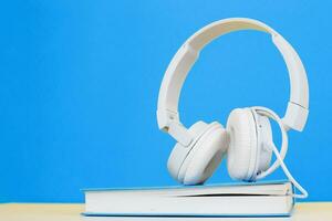 Audio book concept with modern white headphones and hardcover book on a blue background. photo