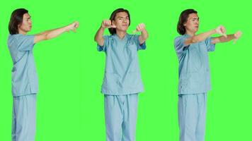 asiatisk specialist som visar tummen ner symbol i studio, ger motvilja och negativitet gest över grönskärm bakgrund. missnöjd medicinsk sjuksköterska uttrycker oenighet, ogillande. video