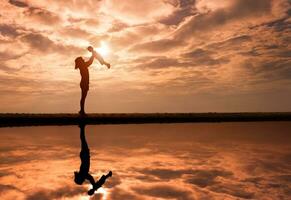 Reflection of Silhouette mother lift her toddler against the sunset photo