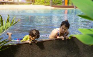 Asian child boy learn swimming in a swimming pool with mom. - Sunset filter effect photo