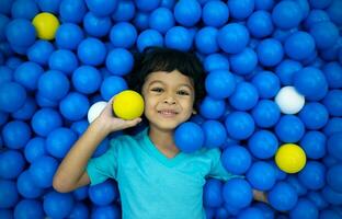 un pequeño asiático chico es jugando con un lote de azul y amarillo pelotas foto