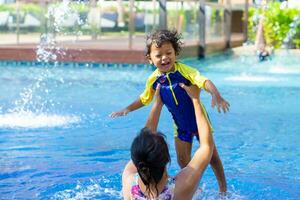 Asian child boy learn swimming in a swimming pool with mom. - Sunset filter effect photo