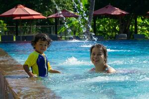 asiático niño chico aprender nadando en un nadando piscina con mamá foto