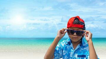 asiático Niños vestir Gafas de sol y verano ropa en un brillante verano mar antecedentes. foto
