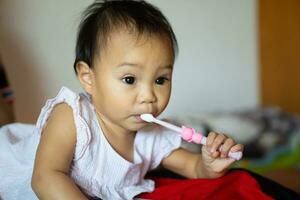 11 meses niña practicando un cepillo de dientes por sí misma desde su de la madre enseñando. foto