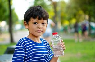 niño sediento agua y sostener transparente el plastico agua botella agua foto