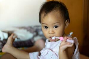 11 meses niña practicando un cepillo de dientes por sí misma desde su de la madre enseñando. foto