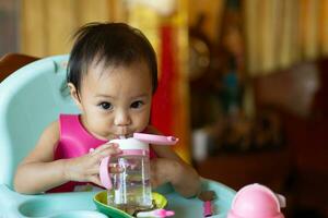 asiático niña 11 meses año antiguo es bebé Bebiendo agua. foto