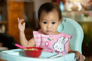 asiático bebé niña 11 meses año antiguo es comiendo alimento. foto