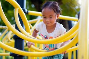 Asian girl is climbing on a playground equipment in a school. photo