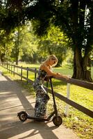 Young woman with an electric scooter in the park on a sunny summer day photo