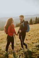 Smiling couple walking with backpacks over green hills photo